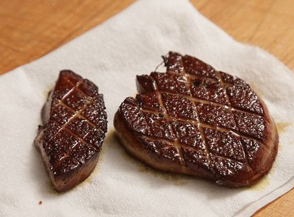 Two pieces of grilled steak with crosshatch grill marks on a paper towel.