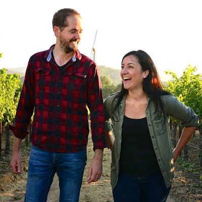 Two smiling people walking through a vineyard, enjoying the Lodi Winegrape Commission's scenic wine country.