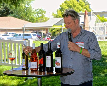Man presenting wine bottles at Lodi Winegrape Commission event outdoors with audience.