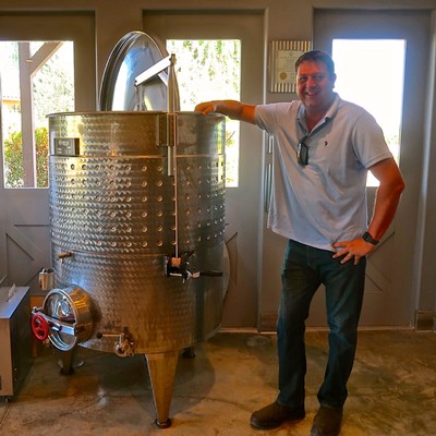 Man standing next to a large stainless steel wine fermentation tank at Lodi Winegrape Commission.