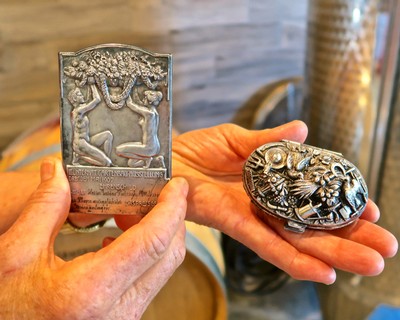Close-up of two detailed silver souvenirs from Lodi Winegrape Commission, showcasing intricate grapevine and wine-related art.