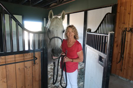 Woman smiling with a white horse in a stable at Lodi Winegrape Commission.