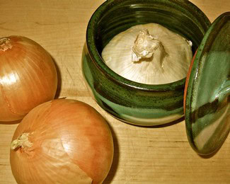 Garlic and onions in a green jar and on a wooden surface, related to Lodi Winegrape Commission.