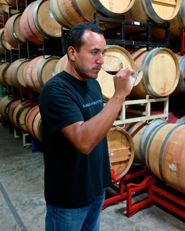 Man tasting wine in a cellar with wine barrels in the background.