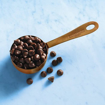 Close-up of dark chocolate chips in a measuring cup on a light blue surface.