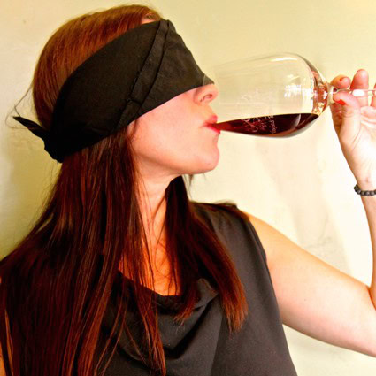 Woman with black blindfold drinking red wine from a glass in a close-up shot.