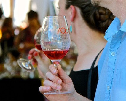 Person holding a glass of red wine at a wine tasting event, focus on the glass and hand, blurred background.