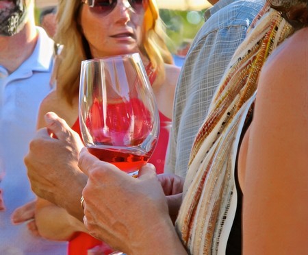 People tasting wine at a Lodi Winegrape Commission event, holding a glass of red wine outdoors.