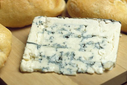 Close-up of blue-veined cheese with bread rolls in the background, representing local food and wine pairings.