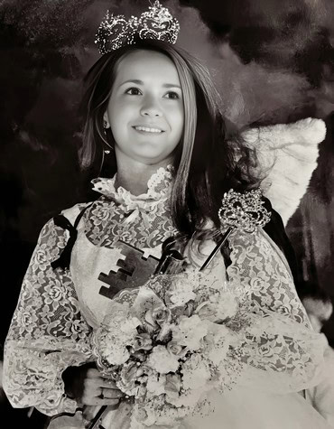 Young girl in a crown and lace dress holding flowers, smiling at a wine industry event.