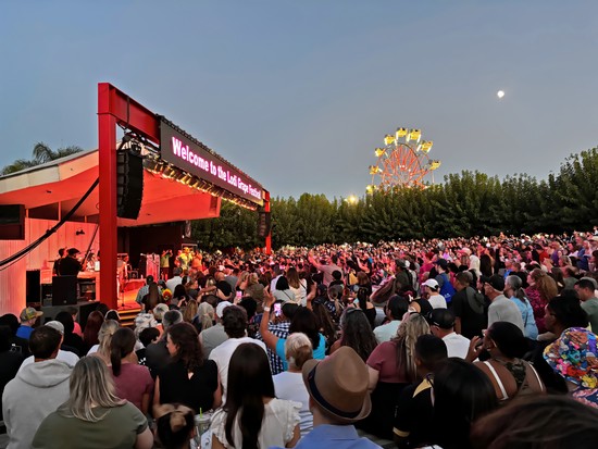 Large crowd attending an outdoor event with a stage, Ferris wheel, and moon in the sky, celebrating Lodi wine and local wineg.