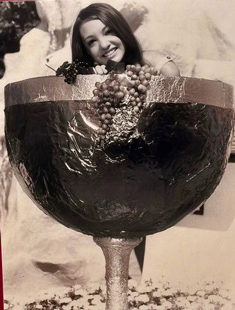 Young woman smiling behind a large wine glass filled with grapes, celebrating wine culture in Lodi, California.
