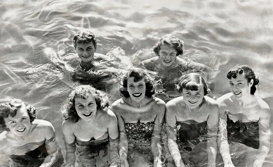 Black and white photo of seven women swimming and smiling in a body of water.