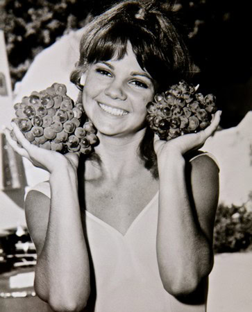 Vintage black and white photo of a woman holding grapes near her face, smiling cheerfully.