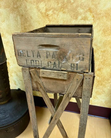 Old wooden crate with faded text on a rustic stand, used for storing wine grapes or related items.