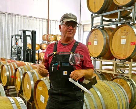 Man tasting wine in a winery with wine barrels in the background, representing Lodi Winegrape Commission activities.
