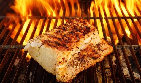 Fresh fish fillet grilling over open flame with charred grill marks and smoky aroma.