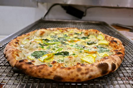 Delicious vegetable pizza with green peppers, zucchini, and melted cheese on a rustic baking tray.