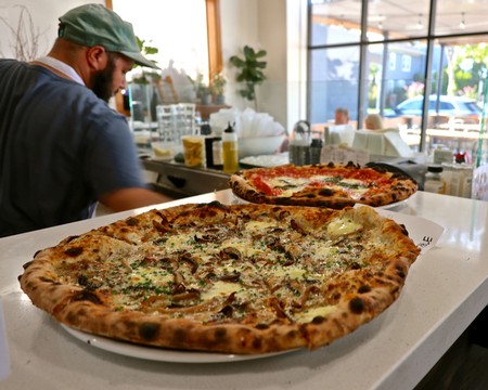 Close-up of two freshly baked pizzas on a white table in a cozy restaurant setting.