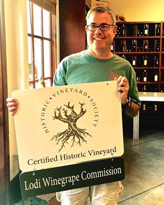 Smiling man holding a sign for the Lodi Winegrape Commission and Certified Historic Vineyard.