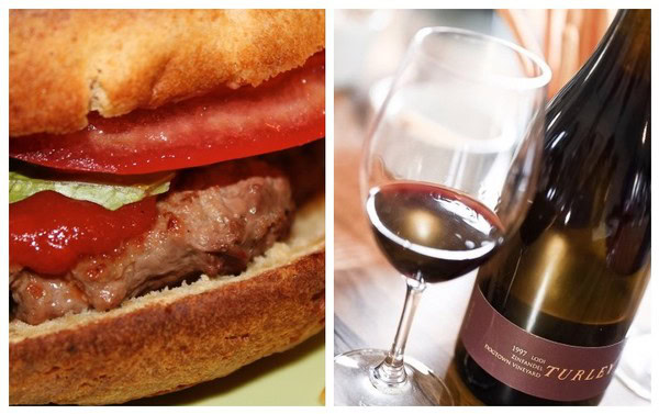 Close-up of a gourmet burger and a glass of red wine with a wine bottle in the background.