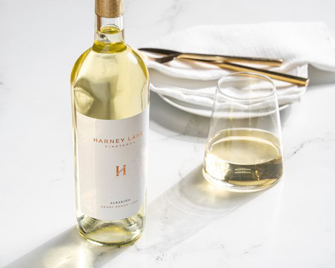 White wine bottle and glass on a white table, representing Lodi Winegrape Commission's wine offerings.