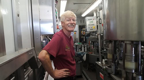 Worker smiling in winery surrounded by industrial wine production equipment.
