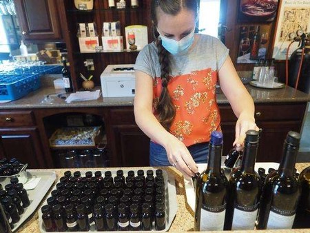 Woman in face mask inspecting wine bottles at Lodi Winegrape Commission tasting room.