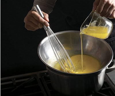 Person pouring lemon juice into a pot while whisking ingredients for cooking or baking.