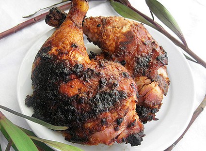 Close-up of grilled chicken thighs with crispy, charred skin on a white plate.