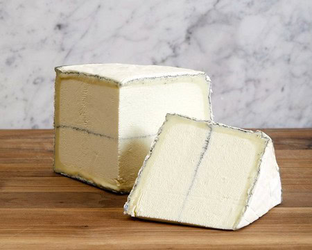 Close-up of a block of creamy Brie cheese with a slice cut, on a wooden surface with a marble background.