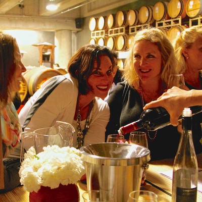 People enjoying wine tasting at a Lodi Winegrape Commission event with barrels in the background.