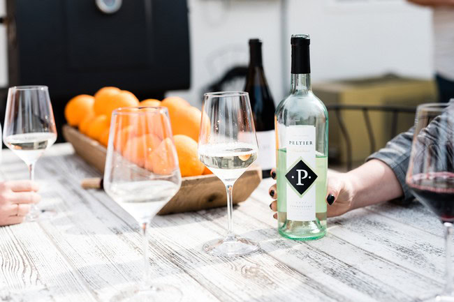People enjoying wine tasting with glasses of white and red wine, and a bottle on a rustic table with oranges in the basket.