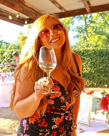 Woman with red hair and sunglasses holding a wine glass at Lodi Winegrape Commission event.
