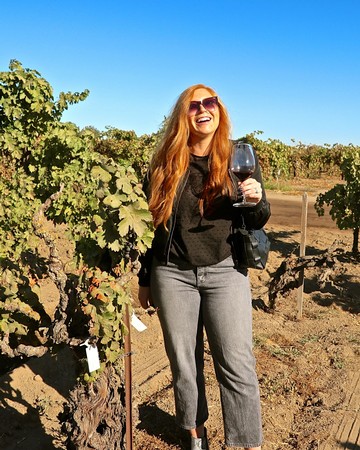 Woman enjoying wine tasting in a vineyard with a glass of red wine on a sunny day.