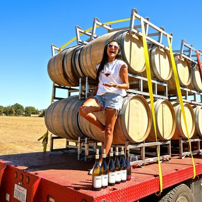 Woman standing next to stacked wine barrels and bottles at a vineyard in Lodi, California.