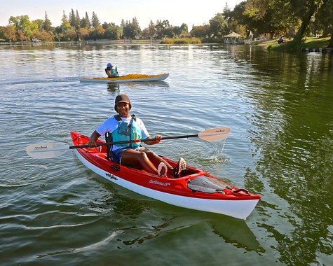 Person kayaking on a peaceful river with trees and a park in the background, enjoying outdoor recreation in Lodi.