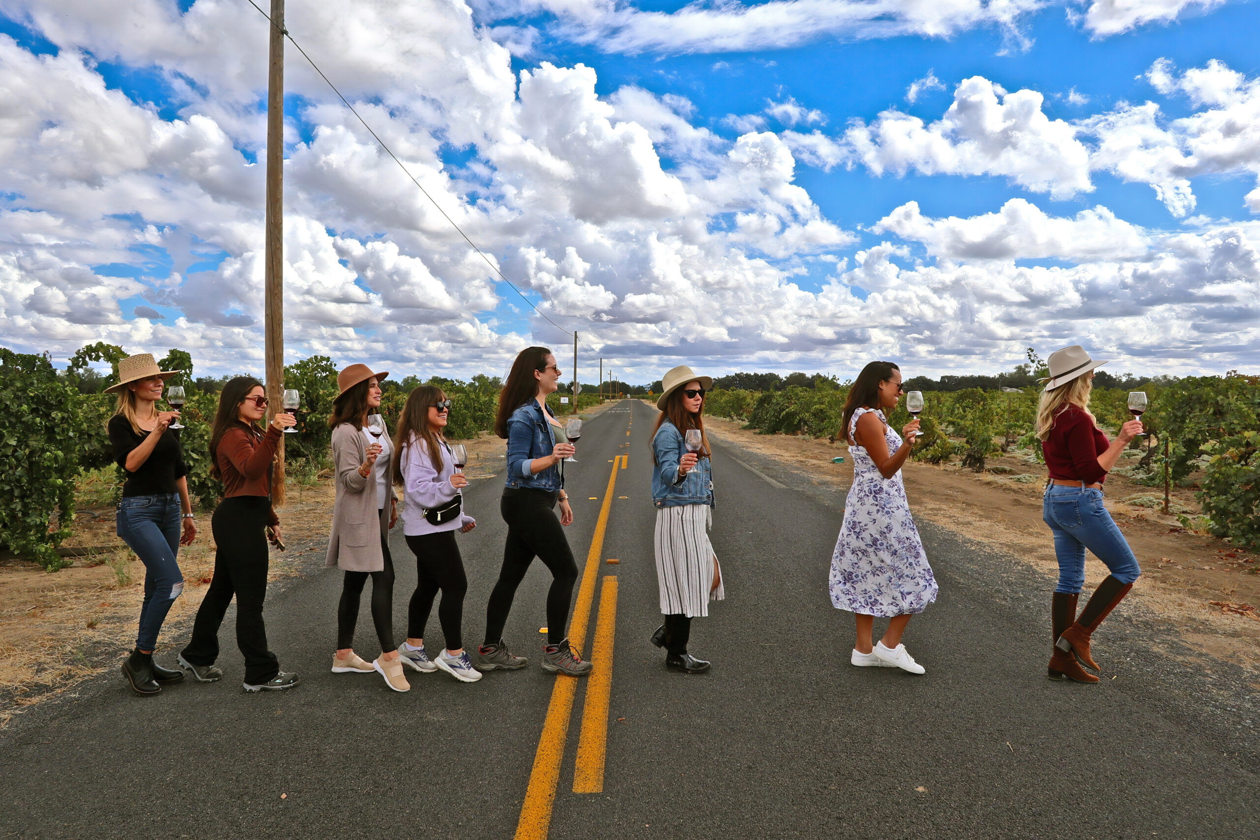 Group of women walking in a line across a rural road in Lodi wine country, enjoying a wine tour.
