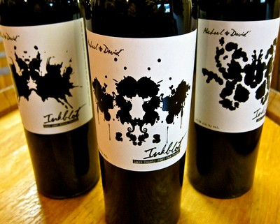 Three wine bottles with artistic black ink splatter labels from Lodi Winegrape Commission on a wooden surface.