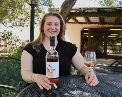 Woman smiling with rosé wine bottle and glass outdoors in a garden setting.
