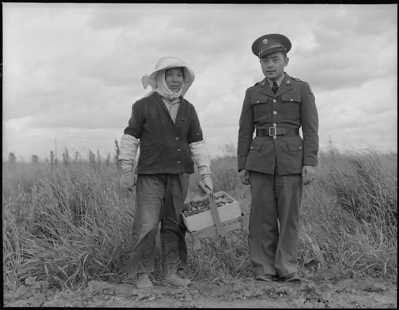 Black and white photo of a woman and a military officer standing in a field with tall grass.
