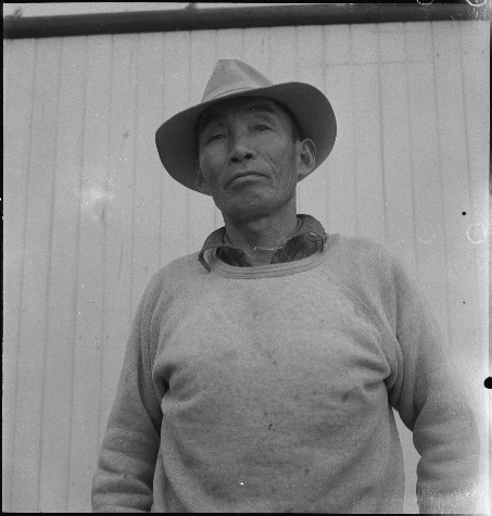 Black and white photo of an elderly man wearing a hat and sweater, standing outdoors.