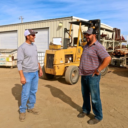 Two vineyard workers in casual attire talking near a forklift at a Lodi vineyard.