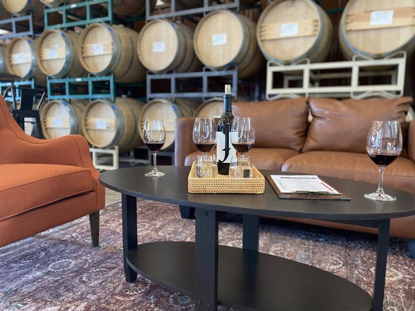 Wine tasting setup with wine bottles, glasses, and a wine bottle on a table in a wine cellar.