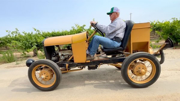 Man driving a vintage tractor in a vineyard, promoting Lodi Winegrape Commission.