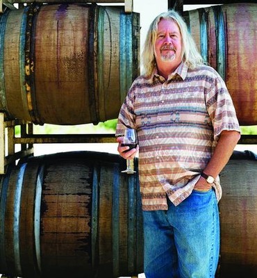 Man enjoying wine tasting at Lodi Winegrape Commission vineyard with wine barrels in background.