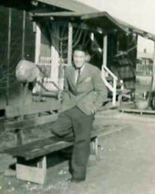 Black and white photo of a man in a suit standing next to a wooden structure at a vineyard.