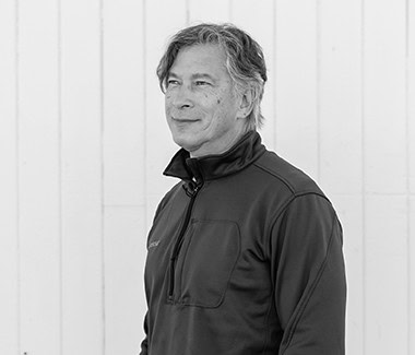 Portrait of a middle-aged man in a black jacket, smiling softly, against a plain background.