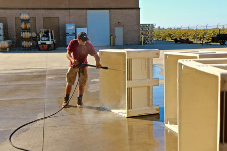 Worker cleaning large wine bottles with a pressure washer at Lodi Winegrape Commission facility.