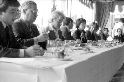 Group of people attending a formal meeting at a long table with wine glasses and documents.